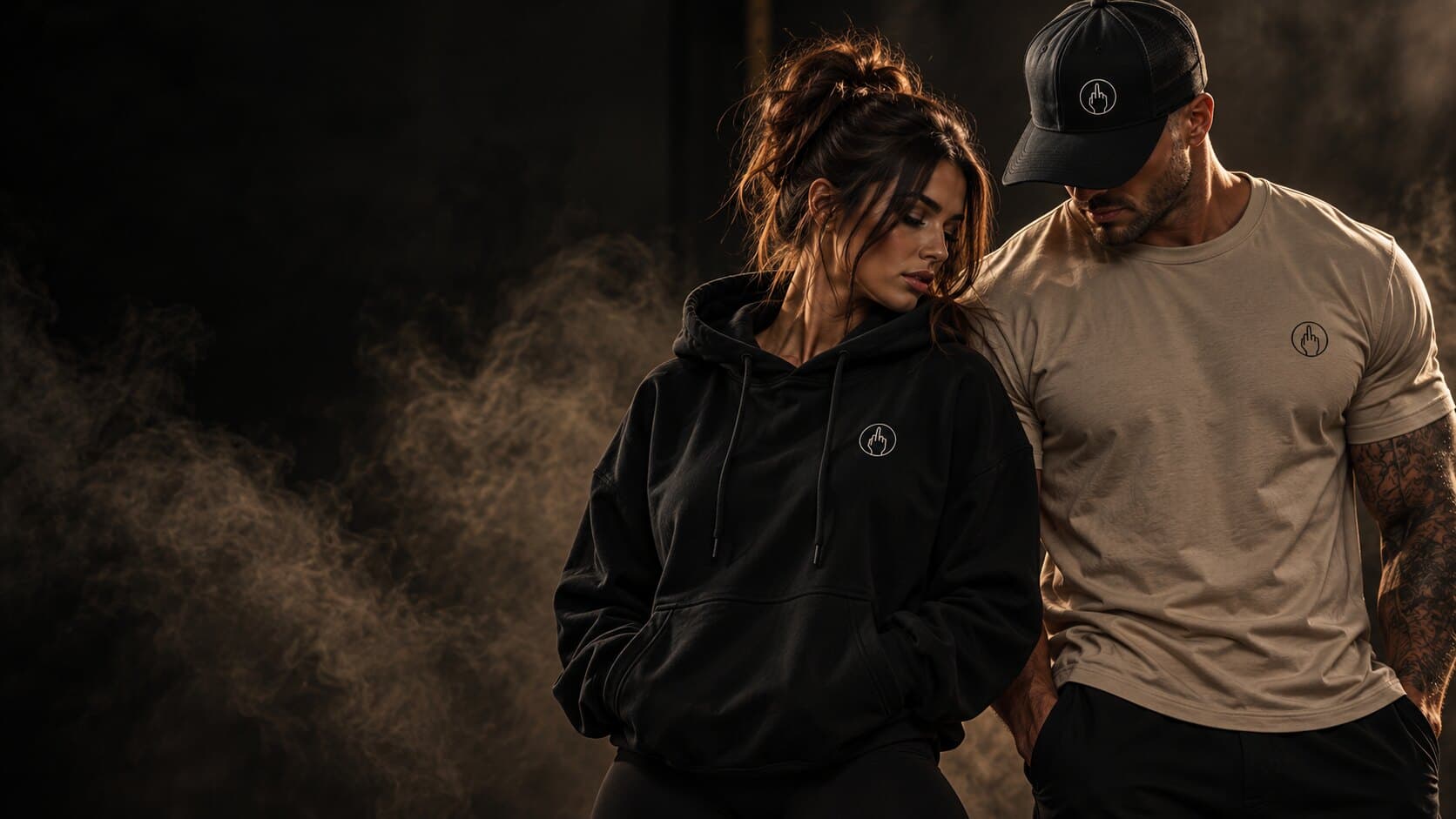 Two Middlefinger Collective models in a black hoodie, sand tee and black cap, each with the hand-in-circle icon